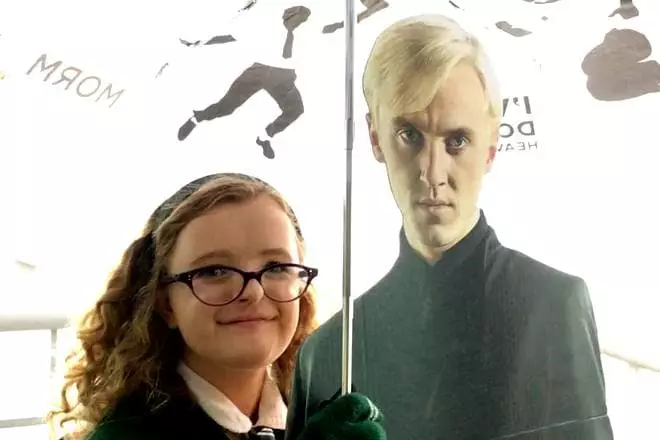 Millie Shapiro na pozadí plakátu s Tomem Feltonem jako Draco Malfoy